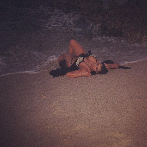 Kim Kardashian in a bikini laying on her back on a sandy beach