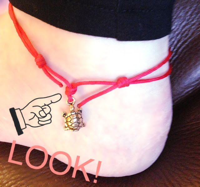 A picture pointing to a small metal turtle on an anklet which is attacked to an ankle