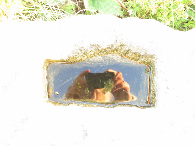 Hands holding camera and blue sky reflected in water on large cube of Portland stone.