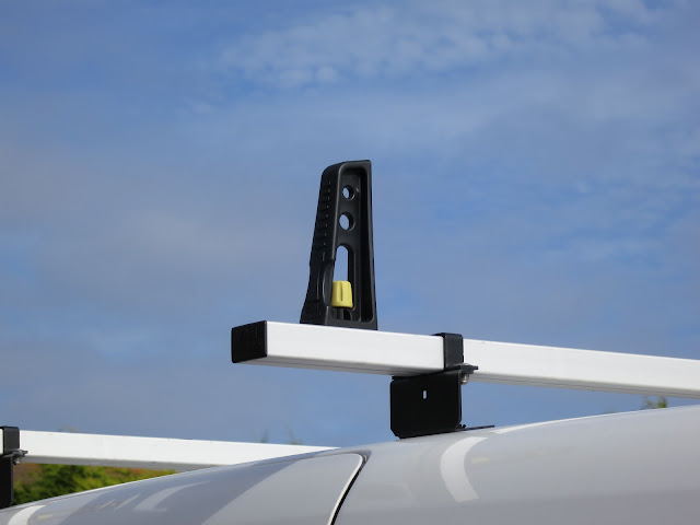 End poles of roof rack on a white van against a blue sky with hints of clouds