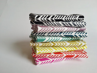 Fabric lined up like books on a shelf in rainbow order featuring arrow feathers print