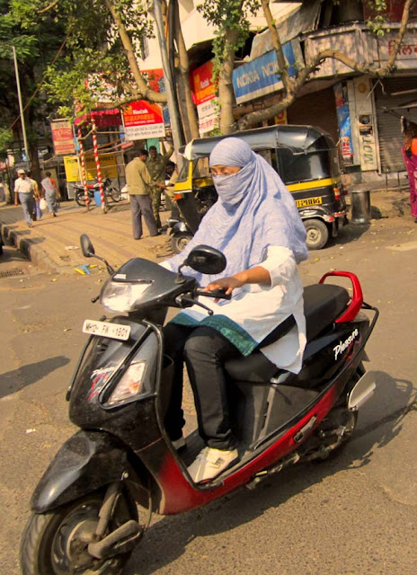 young woman wearing a scarf mask while riding a scooter in Pune