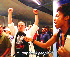 No gif: Uma mulher negra com o microfone esticado para um monte de gente branca passando como que numa manifestação, é como se ela tivesse cantando como nas falas de protesto "alguma pessoa negra?" 