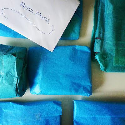 Selection of items wrapped in blue and teal tissue paper, laid out on a tabletop with an envelope on top addressed to Anna-Maria
