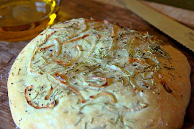 loaf of Focaccia with Onion and Rosemary with olive oil in the back ground