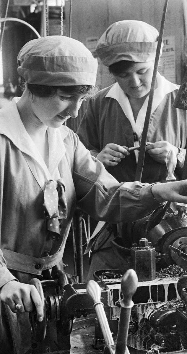 “Two young women operate machinery in the works of Armstrong Whitworth’s and Co,” by Unknown.
