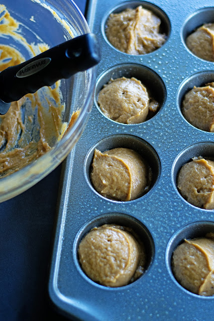 The muffin batter, scooped out, into a muffin pan with the empty batter bowl beside it. 