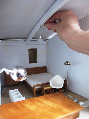 Woman holding a miniature light up to the ceiling of a dry-fitted modern miniature doll's house shed.