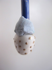 White dolls' house vase, with the end of a paintbrush blu tacked into it and painted with gold spots.