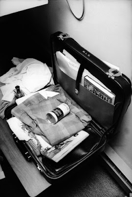 Black and white photo of an open briefcase with folded pajamas and a can of shaving cream on top