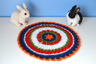 Two resin model bunnies flank the mandala made in Dutch colours: orange, red, white and blue.  Rings of red cluster stitches represent tulips with a touch of green beneath them for the foliage.
