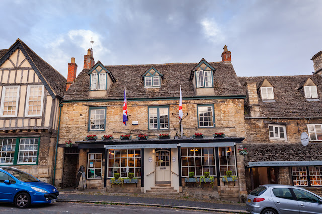 Historic building on the sloping street of Burford in the Cotswolds by Martyn Ferry Photography