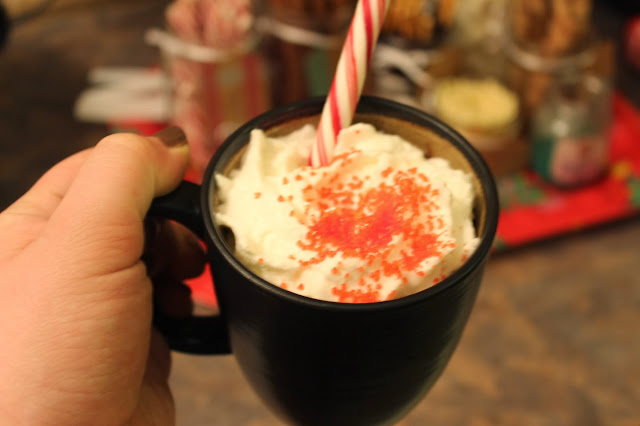 The perfect mug of warm, creamy hot chocolate topped with whipped cream, sprinkles, and a peppermint stick