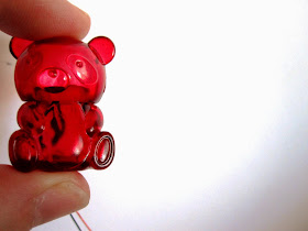 A miniature red plastic bear container held between two fingers.