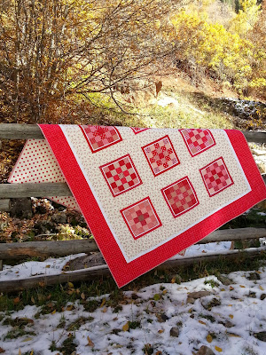 Red an all red quilt draped over a split log fence