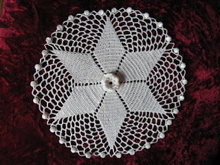Top view of Irish Rose jug cover worked in white size 20 cotton thread. It is edged with glass beads to weigh it down and prevent it from slipping off the top of a jug or cup.  The star shape is made of Australian/UK treble stitches and the centre motif is an Irish rose.