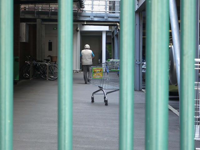 A woman walks through bleak, barred area where there are shopping trolleys and bikes.