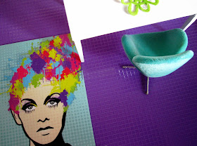 Modern dolls house white table, swan chair, colourful postcard and purple tiled floor:view from above.