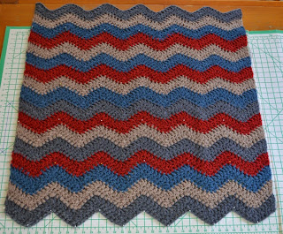 Speedy Ripple Blanket on blocking board. Chunky yarn, 6-ripple stripes in grey, beige, blue and red.
