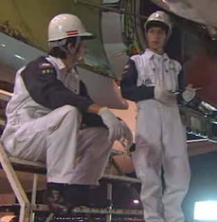 Nakahara talks to Watanabe while performing maintenance.