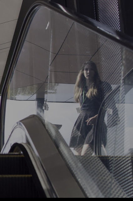 Photo showing upwards escalator with a young lady reflected off the glass side