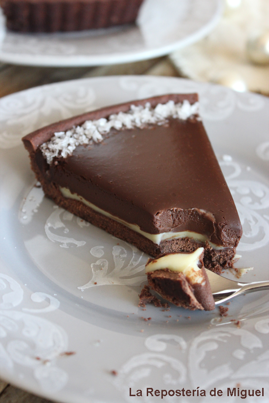 Una porción de tarta de chocolate sobre un plato a la que le falta un par de cucharas y y en la que se aprecia las diferentes capas de chocolate y una textura suave y muy apetecible. 