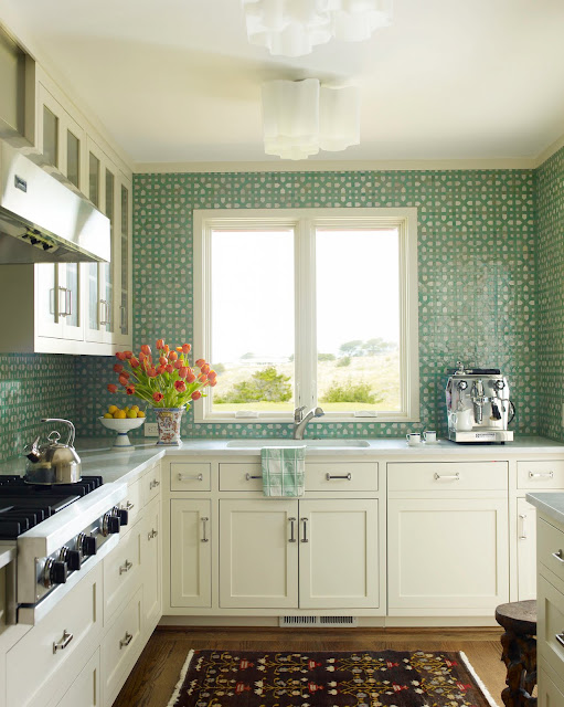 A white kitchen with aqua mosaic tiles from counter to ceiling backsplash, wood floors and stainless appliances
