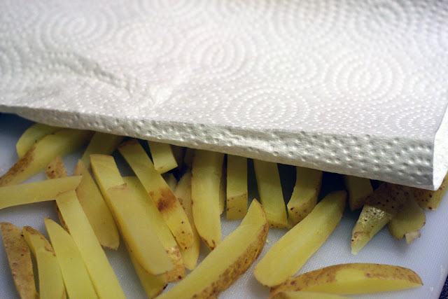 Using paper towel to dry boiled potato fries on a cutting board.