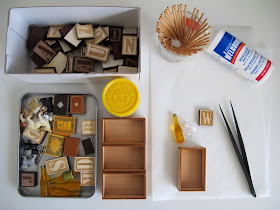 Selection of crafting supplies laid out on a table. Included are tweezers, glue, toothpicks, tiny wooden boxes, letter tiles and vintage dolls' house miniature items.