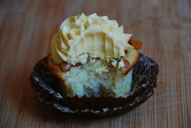 close up of unwrapped cupcake in brown wrapper with swirl of white icing on top with a bite taken out of it