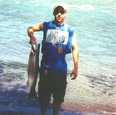 Young man standing on a bank of a river holding up a 12-;pound steelhead he just landed