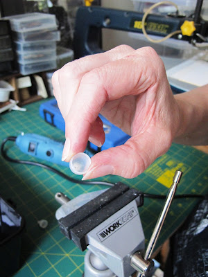 Woman holding a modern miniature lamp shade in front of a vice on a workbench.