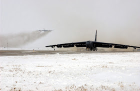 A B-52 Stratofortress taxis down the runway while another B-52 takes of in the background.