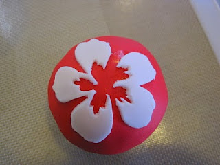 red fondant cupcake with white hibiscus fondant cutout partially transferred onto it