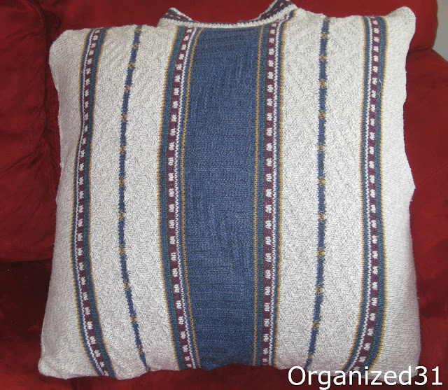 close up of light grey, blue, maroon and green striped sweater pillow on red chair