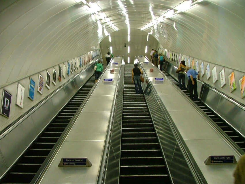 perspective from the bottom of the Tube escalators looking up, with eye level advertising either side.