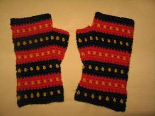A pair of fingerless mitts in Adelaide Crows' colours. They have horizontal stripes, alternating navy and red. Each stripe has a row of yellow dots centred horizontally on the stripe. For example, starting at the cuff the colours are solid navy, yellow dots against the navy, solid navy; solid red, yellow dots against the red, solid red; and so forth ending with a row of solid navy at the fingers.