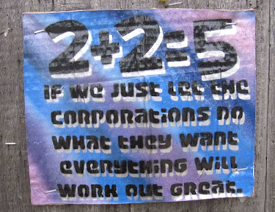 Corrugated cardboard sign, spraypainted purple and blue stripes, with black words 2+2=5 If we just let the corporations do what they want everything will work out great
