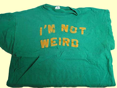 Green shirt with gold block letters reading I'M NOT WEIRD