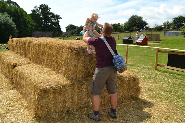 Mr Tin Box catching Tin Box Tot as she jumps off the top of a pile of hay bales