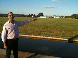 a man standing in front of a pond with a building in the background