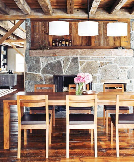 Rustic dining room in a converted barn with wood floors, flagstone fireplace, long wood table, and simple chandelier