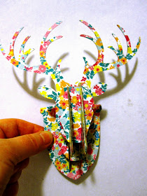 A hand holding up a miniature cardboard stag head, printed with a flower pattern.