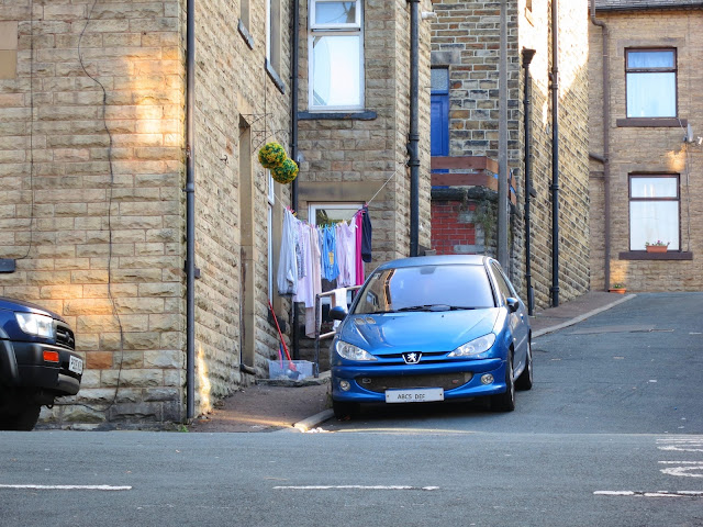 Blue car outside house on a hill with washing outside.