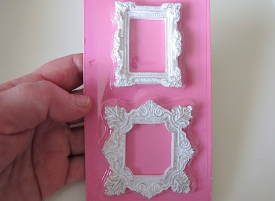Hand holding two white scrapbooking frame embellishments.