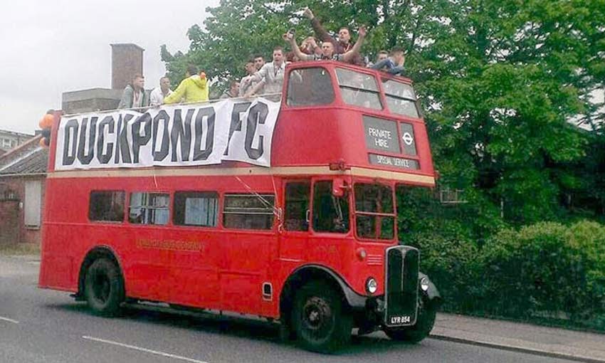 Old school double decker bus, banner states DUCKPOND FC with the team cheering from the open top.