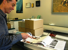 Man in a printers, pointing at two magazine issues.