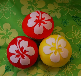 red, orange, and yellow fondant covered cupcakes with white hibiscus fondant decoration