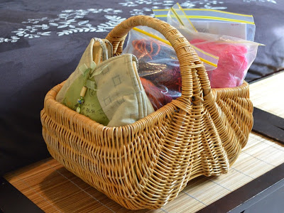 Large rectangular wicker basket with rounded  ends and one central handle containing a collection of crochet project bags.