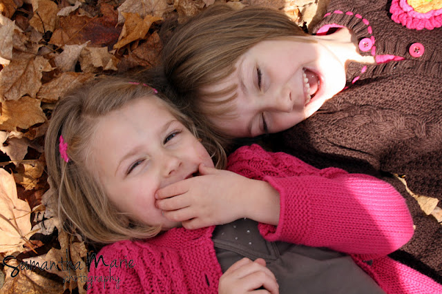 two little girls giggling in fall leaves